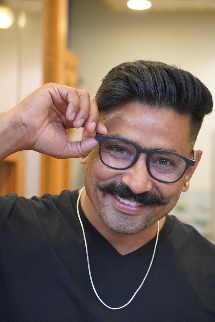Mastering the First Impression: Your intriguing post title goes here Portrait of a cheerful man adjusting his glasses, radiating confidence and style.