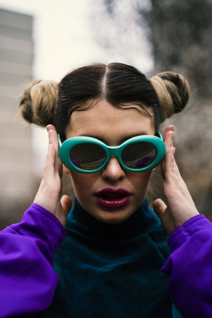 Offerings Stylish woman with unique hairstyle wearing green sunglasses and purple top outdoors.
