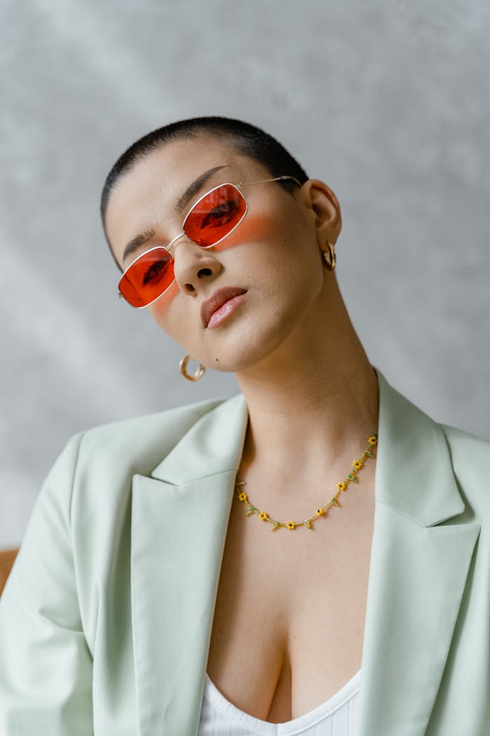 Elegant woman posing with red sunglasses and green blazer, exuding modern fashion.